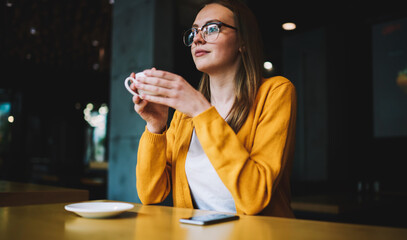 cheerful woman in fashionable apparel looking at camera and enjoying coffee break indoors