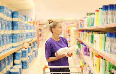 Woman shopping in supermarket reading product information.(washing powder,detergent,shampoo, soap)	