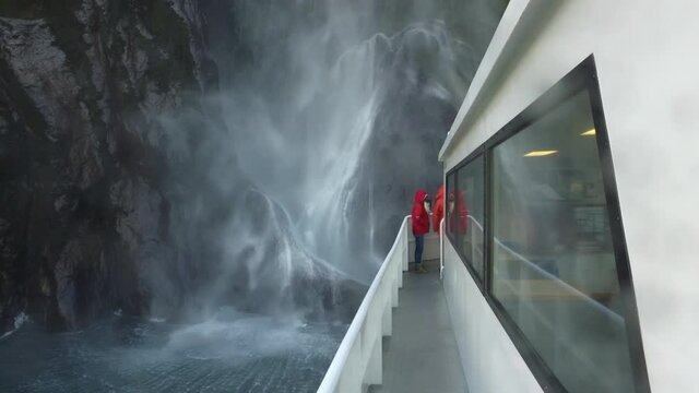 Ladies standing under waterfall on boat in scenic Milford Sound, New Zealand