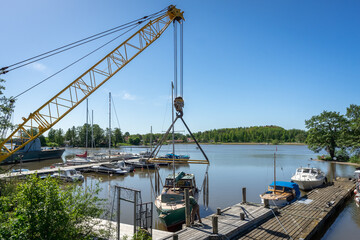 Launching the yacht into the water using a special crane. Wooden pier berth with sailing yachts and boats moored. Every year ship launching transferring a vessel to water. Yachting season opening.