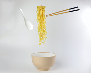 Yellow noodle soup elevated flying suspended in air bowl spoon and chopstick on white background
