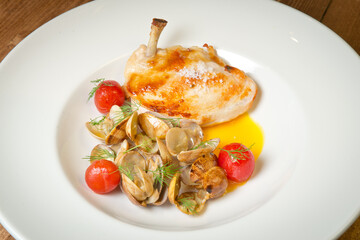 Duck leg with mussels and pickled tomatoes. On a white plate. On a rustic wooden background