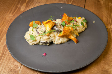 Risotto with wild mushrooms. On a black plate. On a rustic wooden background