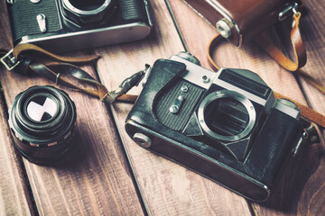 Old vintage film cameras with lense and straps on wooden background.