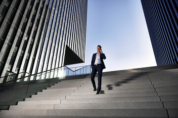 Young and successful businessman walks on a giant staircase between two high-rise buildings and is on the phone. © Marc Zimmermann