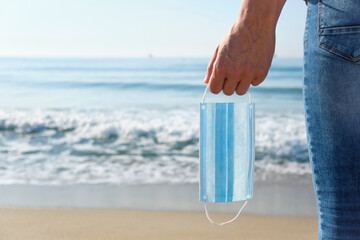 man with a surgical mask in his hand on the beach