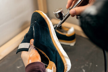 Craft man painting on a pair of shoes. Painting and restoring suede blue sneakers