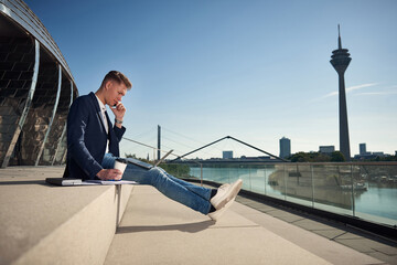 Young businessman sitting in the city outside in the sun we are working and holding a notebook, laptop