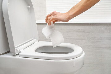 Hand throwing out toilet sheet in bowl
