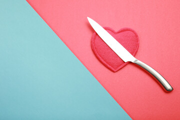 Sharpen steel knife  above red heart like symbol about dangers situation for heard isolated on red and blue background with copy space