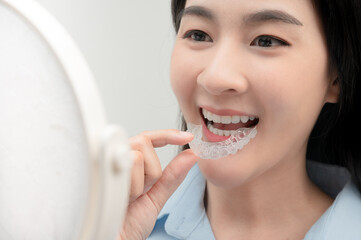 asian woman wareing orthodontic silicone trainer  look her white and Orderly teeth in the mirror happily.