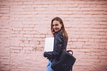 Dreamy hipster girl walking with stylish backpack and laptop device in hand and looking up.