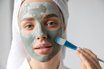 Woman with brush apply clay facial mask. 