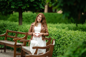 Naklejka premium Beautiful pregnant woman sitting in the park on the bench.