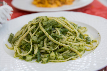 Close up view of a traditional green pasta dish: green Spaghetti with green bean and zucchini, served in a white plate