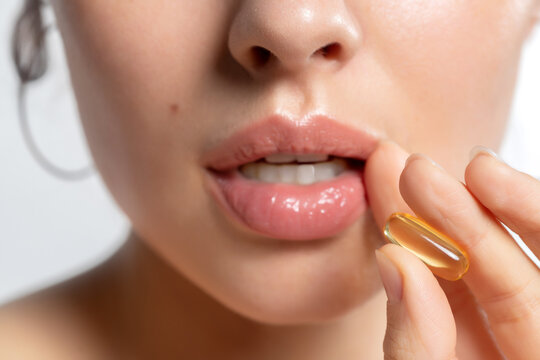 Beautiful  woman hold vitamin fish oil capsule Omega-3 pill in hand near open mouth closeup. 