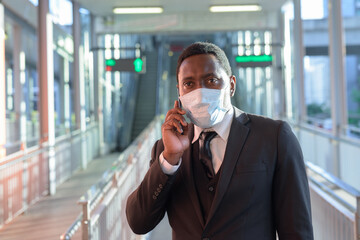 Portrait of African businessman with mask talking on the phone at the train station outdoors