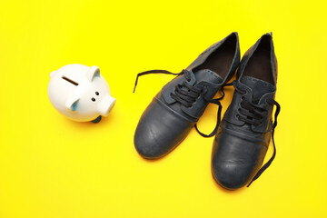 Close up view on small toy piggy bank and black vintage leather shoes isolated on yellow background