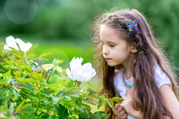 Little girl looking into the flower in green garden or park.