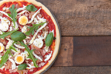 Top view of pizza Italian dish mediterranean food with ham, basil and Rocket green leaves, mozzarella on top with wooden background with copy space.