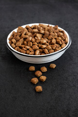 Dry pet food in a white ceramic bowl on black background with copy space