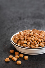 Dry pet food in a white ceramic bowl on black background with copy space