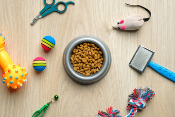 Fototapeta na wymiar Bowl with dry kibble food and cat accessories on wooden table. Top view pet care and training concept. Veterinary shop banner mockup.