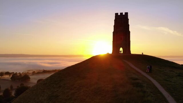 The golden sunrise appearing behind Glastonbury Tor and revealing the misty fields below.