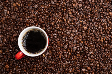 Cup of black coffee from the top on background covered with coffee beans.