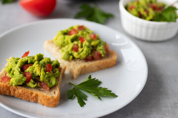 Avocado and chili pepper appetizer on square toasts in a white plate. Close-up.