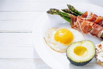 fried asparagus wrapped in jamon, fried eggs, bruschetta with soft cheese and avocado on a white plate
