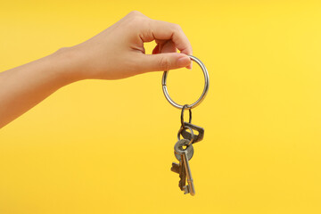 Female hand holding keys on yellow background.