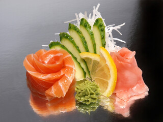 Salmon sashimi with ginger, wasabi, cucumber and lemon on a shiny surface. Japanese kitchen