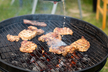 Juicy meat with grilled vegetables (Steak, pork, beef, pepper, salt, grill). The cook pours beer on the juicy meat