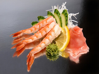 Tiger shrimp sashimi with ginger, wasabi, cucumber and lemon on a shiny surface. Japanese kitchen
