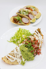 Chicken Quesadilla with Guacamole and Pico de Gallo on a White Plate with Tacos in the Background