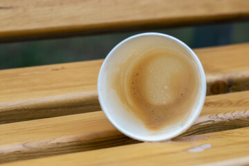 An almost empty glass lies on a park bench and coffee spilled to the surface. Photo from a walk on a warm summer day.