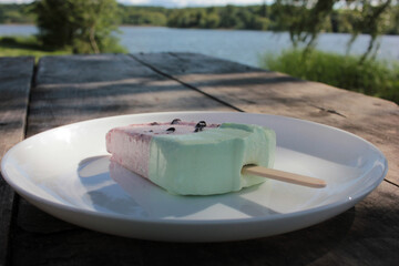 Pink ice cream popsicle in the shape of watermelon on a white plate outdoors. Vintage wooden table...