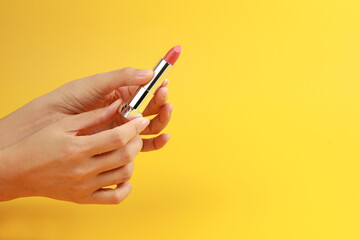 Woman hand holding red lipstick on yellow background.