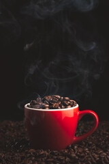 Red Cup with smoking and steaming coffee beans on table covered with coffee beans.