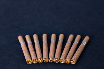 brown cigarettes with a filter are spread out on a background of black textured paper