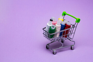 multicolored sewing threads in a mini cart on a background of lilac textured paper