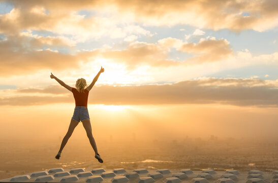 Success and uplifting concept. Happy celebrating woman on the rooftop of skyscraper overlooking the city during a beautiful orange sunrise view. 

