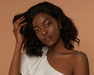 African american girl in white jacket with wavy hair and make-up posing on a beige background. Fashion style closeup studio portrait. Elegant fashionable woman