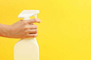 Woman hand holding spray with detergent on yellow background.