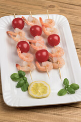 Shrimps with cucumber and tomatoes on skewer in white plate.