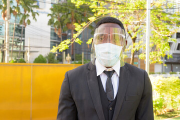 African businessman with mask and face shield at the bus stop in the city outdoors