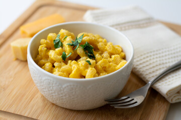 Traditional American macaroni and cheese comfort food (also called mac n cheese) with elbow pasta coated in a cheesy creamy cheddar sauce. Topped with parsley, cheese in the background.
