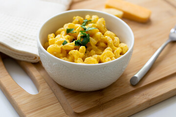 Traditional American macaroni and cheese comfort food (also called mac n cheese) with elbow pasta coated in a cheesy creamy cheddar sauce. Topped with parsley, cheese in the background.
