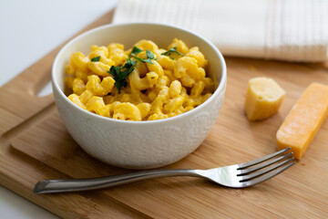 Traditional American macaroni and cheese comfort food (also called mac n cheese) with elbow pasta coated in a cheesy creamy cheddar sauce. Topped with parsley, cheese in the background.
